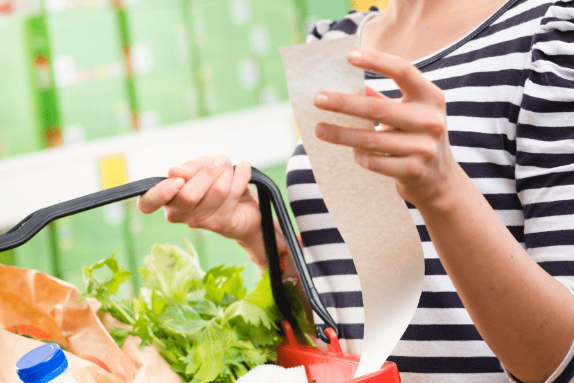 Person looking at their grocery receipt while carrying the basket of groceries.