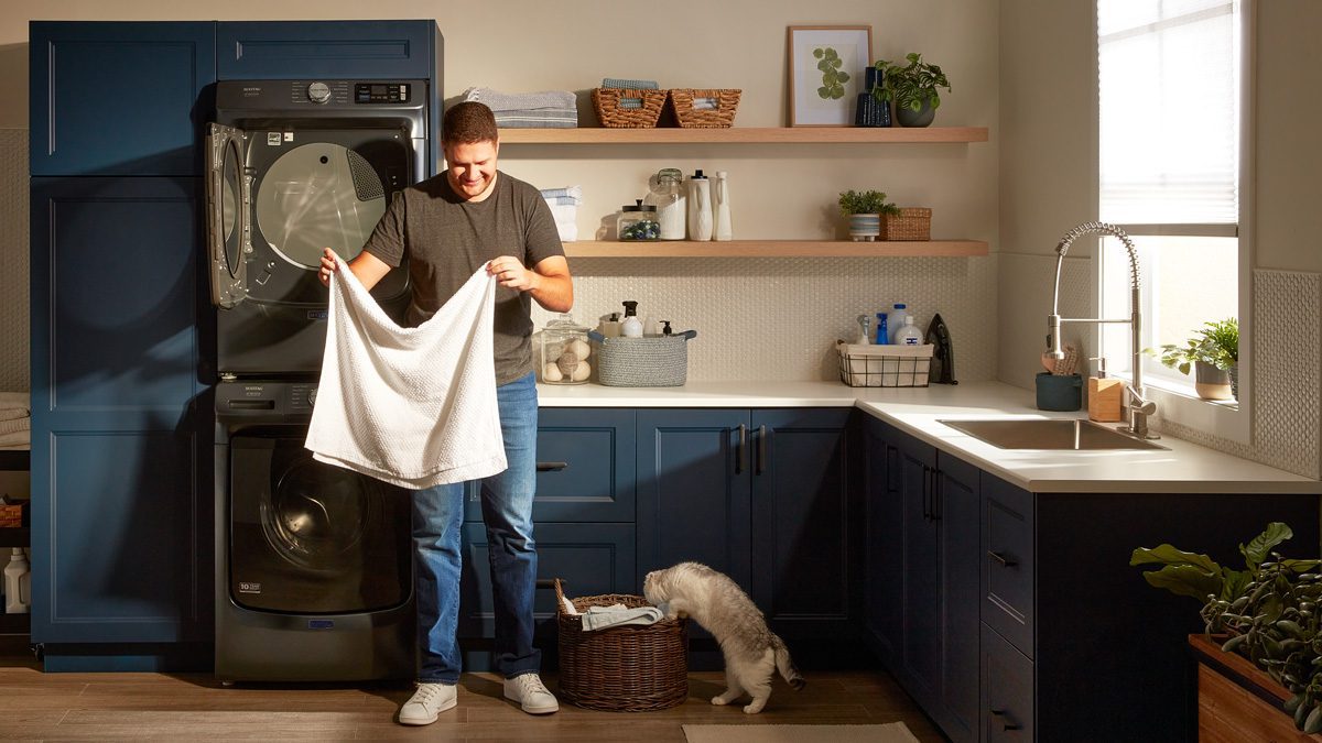 man folding a towel while his cat tries to go into his laundry basket.
