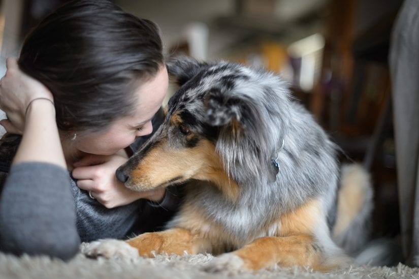 A beautiful moment between a dog and a woman lying on a carpet indoors cuddling