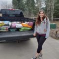 woman stands in front truck with donation of pet food
