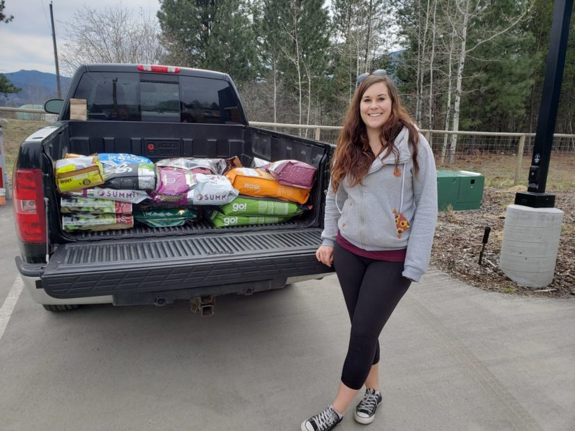 woman stands in front truck with donation of pet food