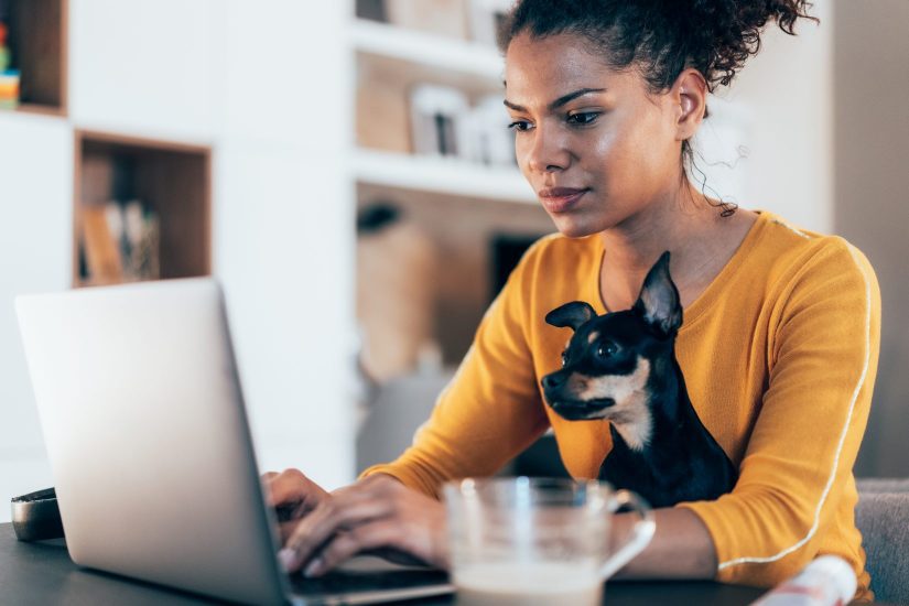 woman working from home with dog in lap whicle working on laptop